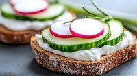 Fresh sandwich with cream cheese, sliced cucumber, radish and rosemary on dark bread. Healthy vegetarian appetizer served on gray background.