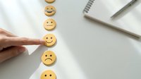 Customer satisfaction survey with hand selecting happy smiley face among emotion feedback icons on white desk background for service rating.