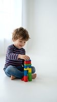 Happy young boy with curly brown hair playing with colorful building blocks while sitting cross-legged on floor wearing striped shirt and jeans.