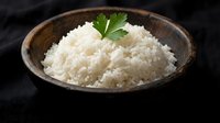 Cooked white rice in rustic wooden bowl garnished with fresh parsley on dark background for culinary and food photography projects.
