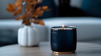 Elegant navy blue textured candle holder with burning flame on wooden surface, white ceramic vase with autumn leaves in soft focus background creates cozy atmosphere.