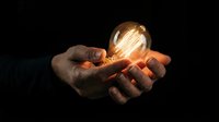Hands gently holding glowing light bulb against dark background symbolizing innovation, creativity, inspiration and bright ideas for business concepts.