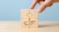 Hand placing wooden block with lightbulb and hands icon representing innovation, creativity and idea protection concept for business solutions.