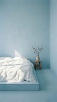 Minimalist bedroom interior with soft blue walls, white bedding on platform bed, wooden stool with dried flowers in ceramic vase, natural light creating calm atmosphere for home decor and design projects.