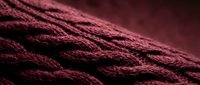 Close-up of burgundy knitted fabric with intricate cable pattern texture. Cozy wool sweater detail showcasing craftsmanship for fashion and textile design projects.