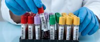 Laboratory technician in blue gloves organizing colorful blood collection tubes with barcodes for medical testing and diagnostic procedures in clinical setting.