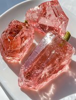 Pink tourmaline raw crystals on white ceramic plate with natural sunlight creating shadows for gemstone collection and mineral specimen display.