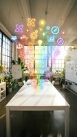 Modern office workspace with white table and colorful glowing icons floating above, including lightbulb, gear, chart, and star symbols. Bright industrial loft with large windows, plants, and creative business environment for corporate design projects.