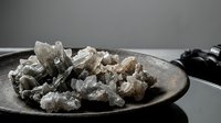 Raw mineral crystals and gemstones collection displayed on rustic ceramic plate for geology study, healing practices, and natural decoration purposes.