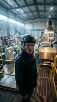 Mature male factory worker wearing safety helmet in industrial manufacturing facility with machinery and equipment for commercial use.