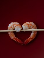 Fresh cooked shrimp arranged in heart shape on chopstick against deep red background, romantic seafood concept for Valentine's menu or date night dining.