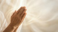 Hands pressed together in prayer position against soft flowing white fabric background creating peaceful spiritual atmosphere for meditation and worship.