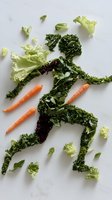 Fresh vegetables arranged in shape of running athlete figure on white background, featuring kale leaves, carrots and lettuce pieces for healthy lifestyle concept.