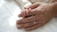 Newborn baby hand grasping adult finger on white fabric, symbolizing family bonding, parenthood, and new life. Suitable for healthcare, family, and parenting content.