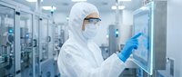 Scientist in protective suit operating touchscreen interface in sterile pharmaceutical laboratory cleanroom facility for medical research and drug development.