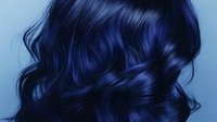 Dark blue wavy hair with shiny highlights flowing in loose curls against black background, professional salon hairstyle showcasing vibrant midnight color and glossy texture.