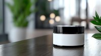 Minimalist black and white cosmetic jar on wooden table with blurred green plants and bokeh lights in background, mockup for skincare product packaging.