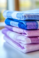 Stack of folded colorful cotton kitchen towels in blue and purple shades with textured weave pattern, perfect for home decor and lifestyle concepts.