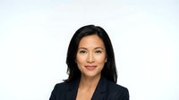 Professional Asian businesswoman in dark suit smiling confidently against white background, corporate headshot for business presentations and marketing.