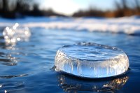 Frozen bubble on water surface creates natural ice ring formation with crystalline texture against blue winter lake. Macro photography captures delicate details.
