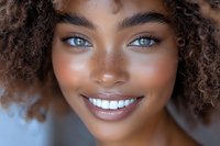 Close up portrait of young African American woman with natural curly hair, bright blue eyes, freckles and radiant smile against light background.
