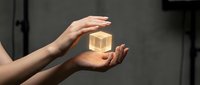 Young woman with fair skin holding a glowing golden cube in her hands against a dark background, representing innovation, technology, and business solutions.