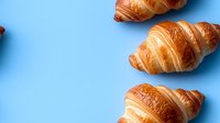 Fresh golden croissants scattered on bright blue background, flaky layered French pastries with buttery texture and crispy crust, food photography.