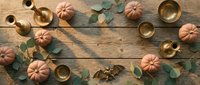 Autumn flat lay with orange pumpkins, golden brass cups and eucalyptus leaves on rustic wooden background for seasonal home decor and thanksgiving styling.