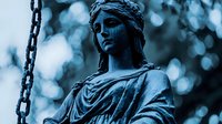 Ancient stone statue of draped female figure with chain against blurred bokeh background in moody blue tones, classical art and architecture element.