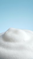 Soft white foam texture close-up on a light blue background, showcasing creamy lather for skincare, cosmetic, or cleaning product concepts.