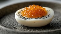 Gourmet deviled egg topped with orange caviar and black poppy seeds on dark ceramic plate. Elegant appetizer for fine dining and culinary presentations.