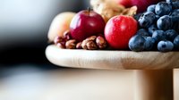 Fresh seasonal fruits and nuts arranged on wooden cutting board for healthy eating and cooking preparation in modern kitchen setting.