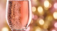 Sparkling rosé champagne glass with bubbles against golden bokeh lights background for celebration and festive occasions.