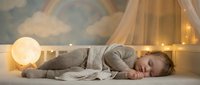 Peaceful toddler sleeping in a cozy crib with a glowing moon lamp and rainbow mural, warm fairy lights creating a dreamy nursery atmosphere.