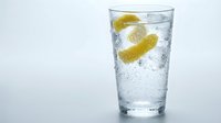 Refreshing glass of sparkling water with ice cubes and fresh lemon slices on white background, isolated for beverage, wellness and drink design projects.