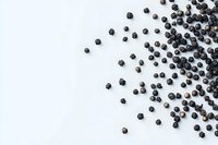 Black peppercorns scattered on white background creating diagonal composition with copy space for text, food photography styling.