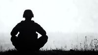 Silhouette of military soldier crouching on hilltop against moody sky, dramatic black and white composition showing solitude and contemplation in wartime setting.