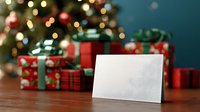 Blank greeting card mockup with Christmas gifts and decorated tree with bokeh lights in blurred background on wooden table.