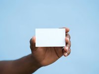 Hand holding blank white business card against clear blue background, ready for custom branding and marketing designs.