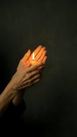 Mature adult hands cradling a glowing candle flame against dark background, symbolizing hope, spirituality, and compassion for memorial, charity, or wellness concepts.