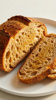Freshly baked artisan sourdough bread with airy crumb structure sliced on white plate, rustic bakery loaf with golden crust for food photography and culinary content.
