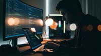 Software developer programming at night with multiple monitors displaying code in dark office environment with bokeh lights.