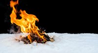 Dramatic campfire burning brightly in white snow against dark background creating striking contrast between fire and winter elements.