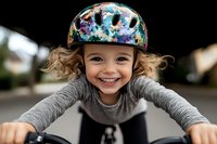 Joyful young girl with curly hair wearing colorful safety helmet while riding bicycle, expressing pure happiness and excitement during outdoor activity. Natural lifestyle moment.
