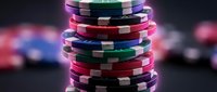 Colorful casino poker chips stacked in tower on dark background with blurred gaming elements. Gambling entertainment concept for betting industry designs.