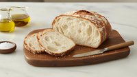 Fresh artisanal sourdough bread sliced on wooden cutting board with olive oil and sea salt, showing airy crumb texture and crispy golden crust.