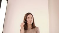 Young brunette woman applying mascara makeup in modern bathroom mirror reflection morning beauty routine skincare cosmetics lifestyle.