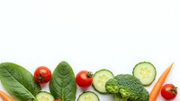 Fresh organic vegetables including broccoli, cherry tomatoes, cucumber slices, spinach leaves and carrots arranged on white background for healthy eating.