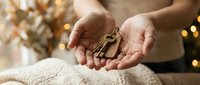 Woman hands holding house keys in cozy home interior with warm lighting and festive decorations, real estate concept for new homeowners celebration.