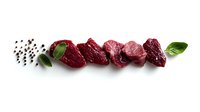 Raw beef tenderloin pieces arranged in row with black peppercorns and fresh basil leaves on white background, isolated food composition for menu design.